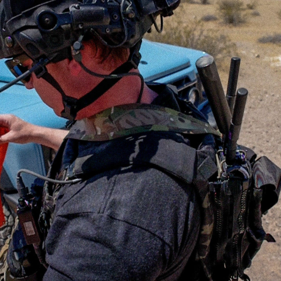 Person in military gear holding an orange flag in a desert setting