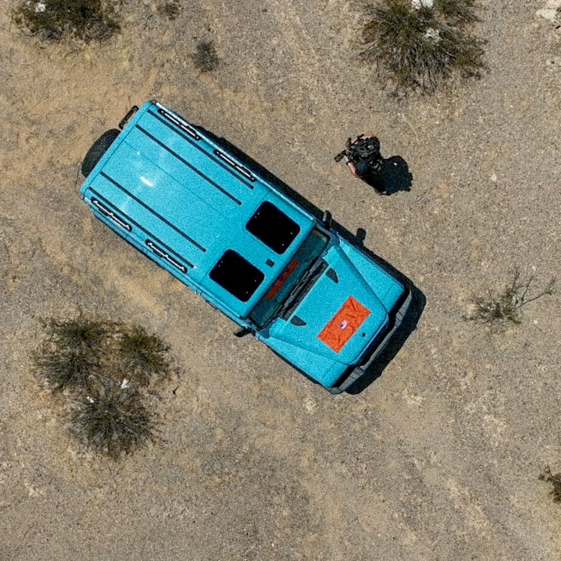 Aerial view of a blue truck in a desert landscape with sparse vegetation.