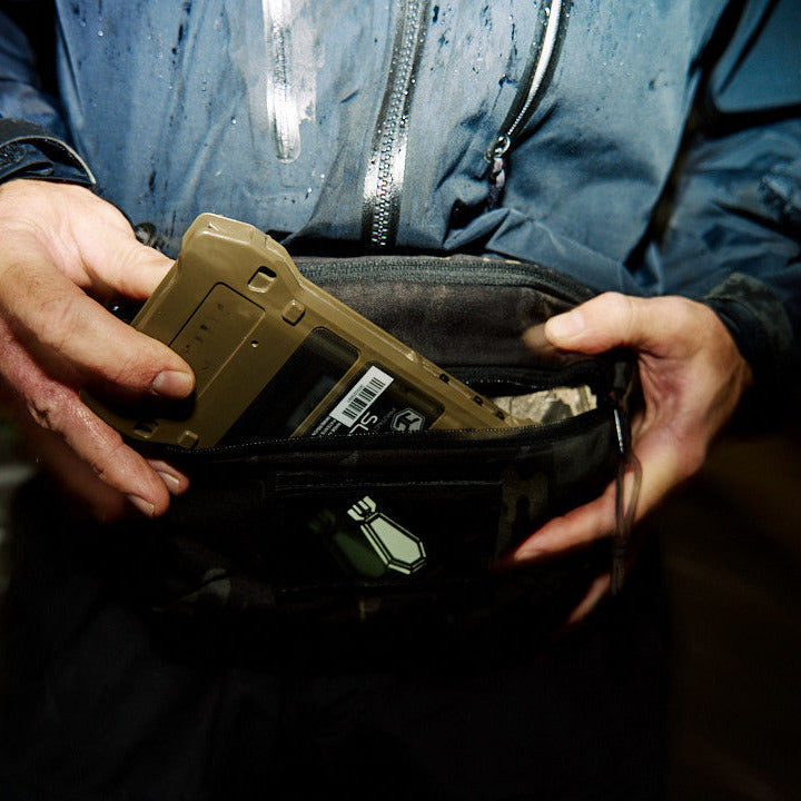 Person holding a black bag with a green device inside, dark background