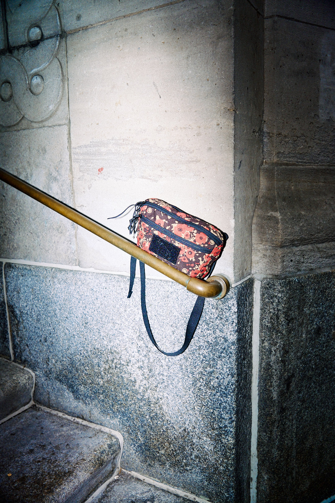 Floral-patterned bag hanging on a metal railing against a concrete wall.