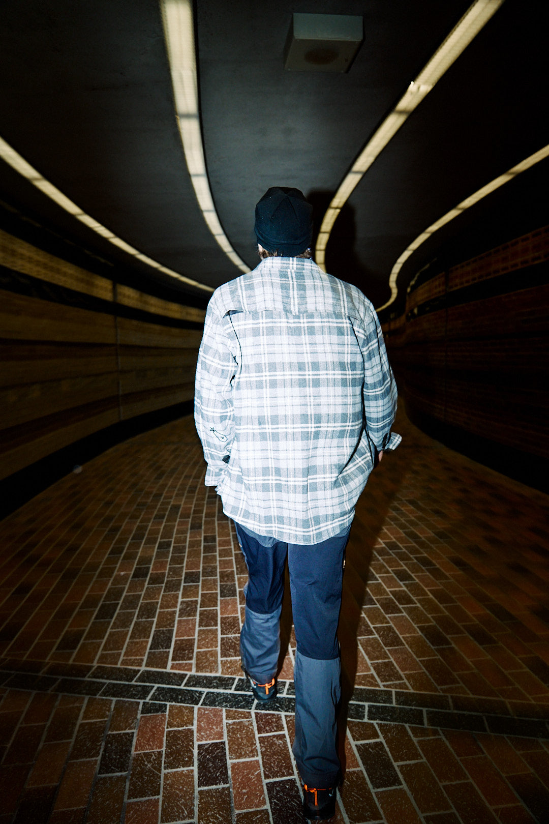 Person walking through a dark, curved hallway with tiled floor
