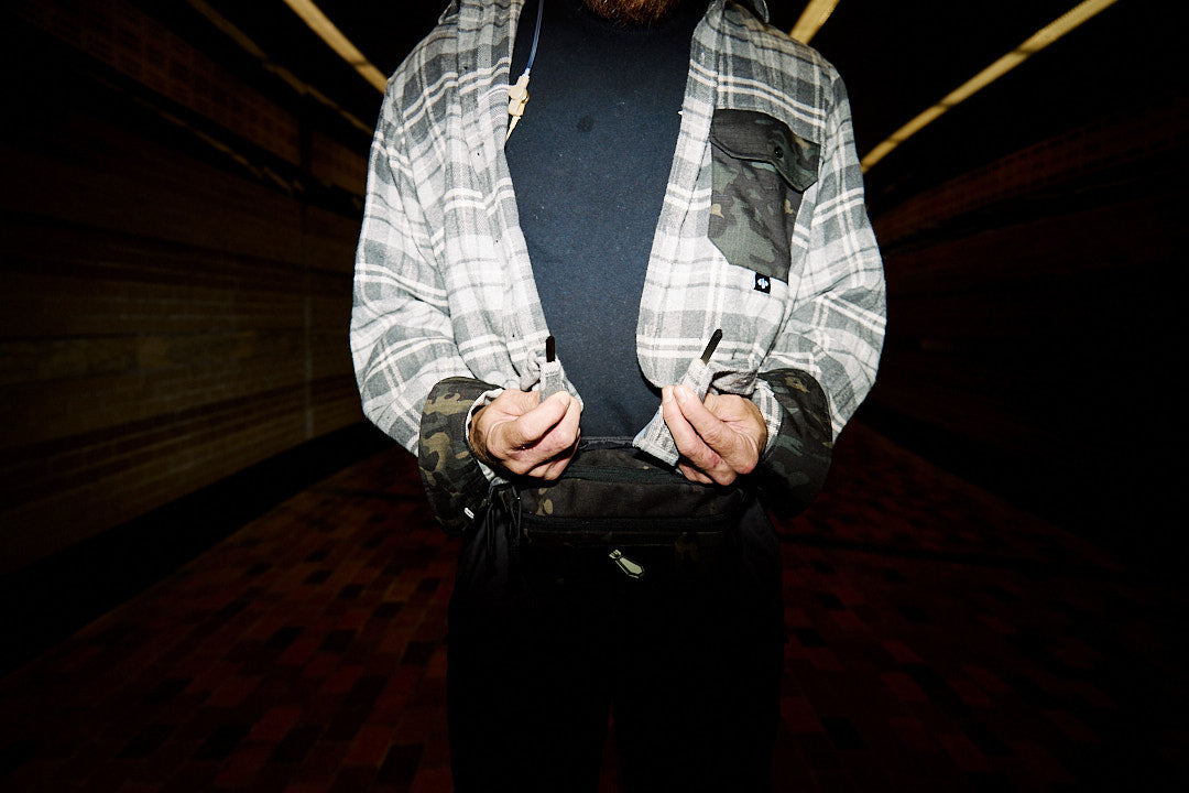 Person wearing a plaid shirt with camouflage sleeves in a dimly lit room.