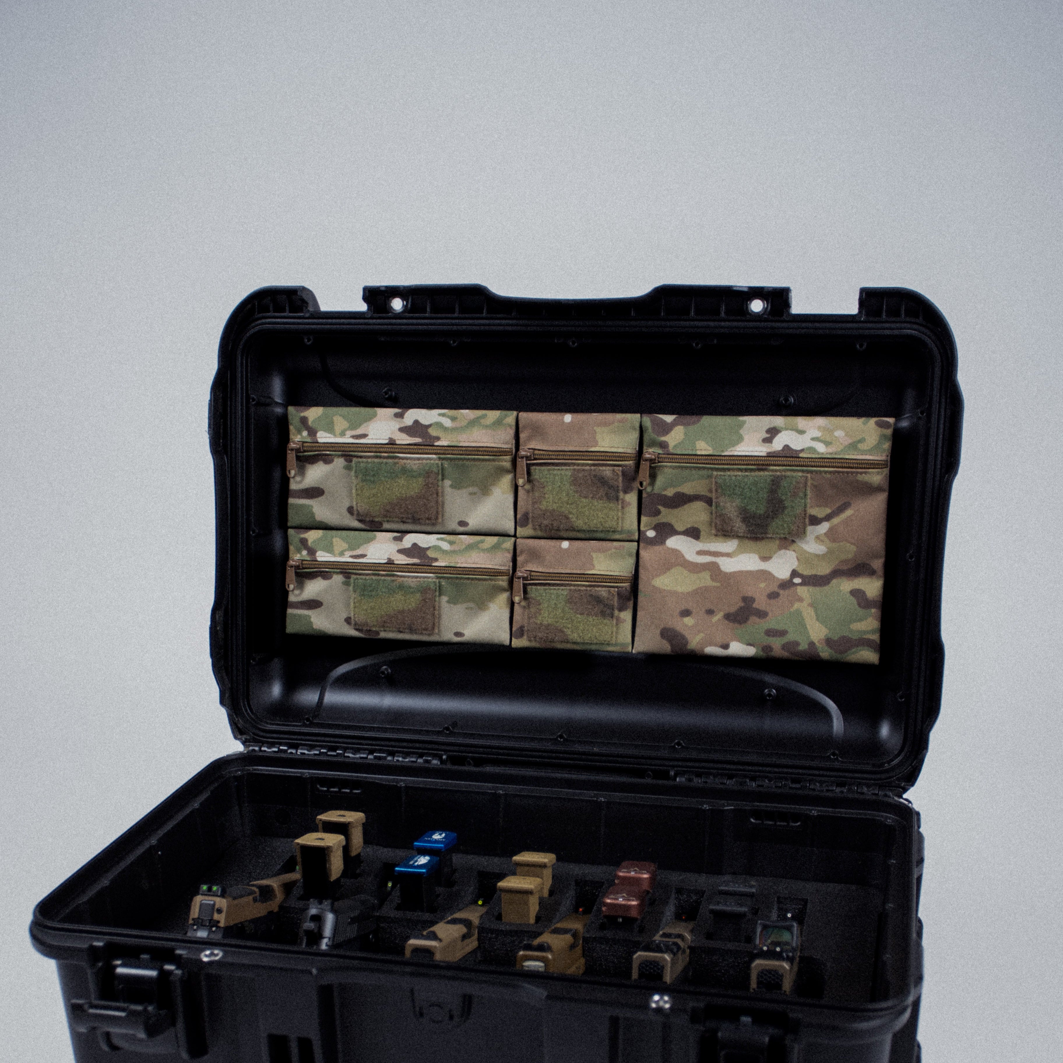 Black hard-shell case with camouflage interior and various items on a gray background