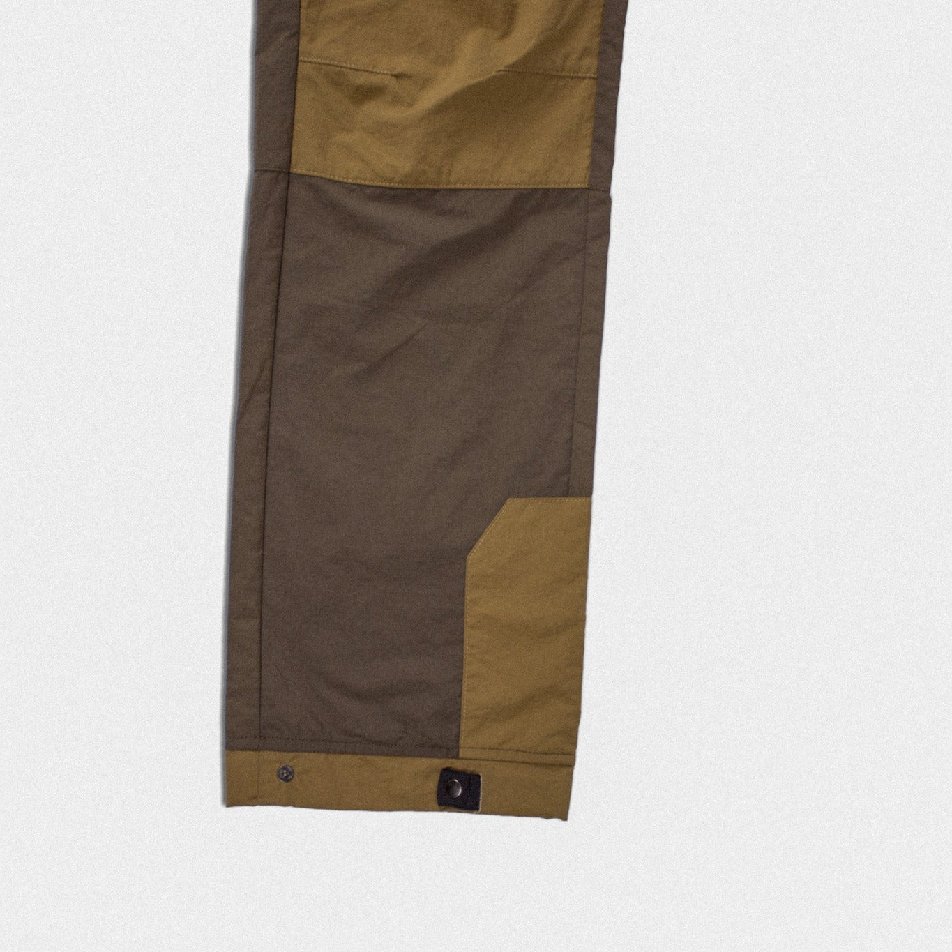 Close-up of a jacket sleeve showing color-blocked panels in olive green and dark brown on a light gray background.
