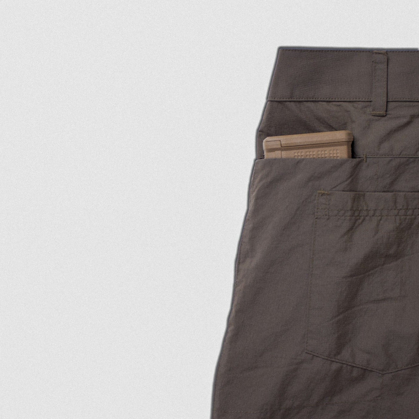 Close-up of a dark brown garment, showing a side pocket with a beige tag or insert, photographed against a plain light gray background.