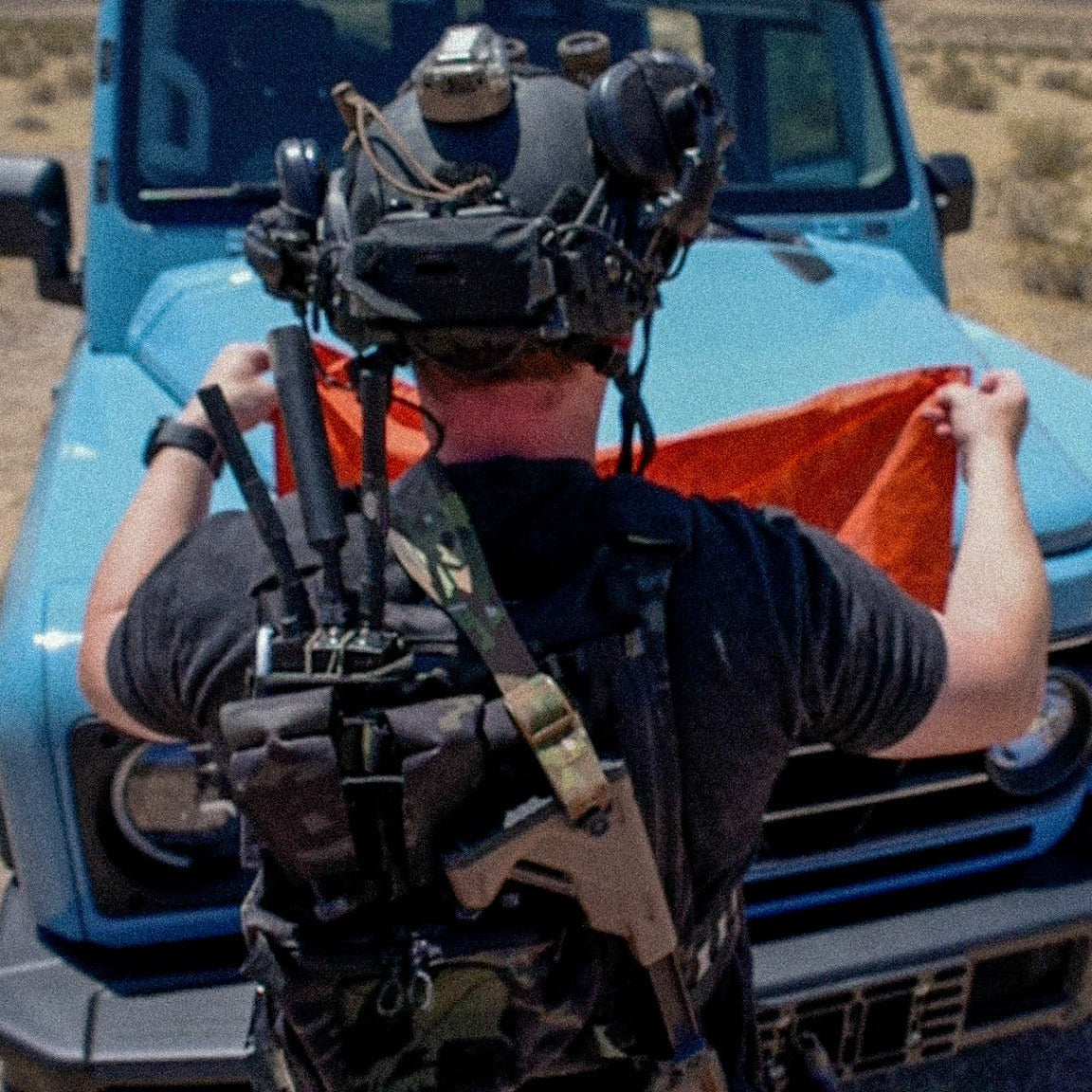 Person with VR headset and backpack in front of a blue truck in a desert setting
