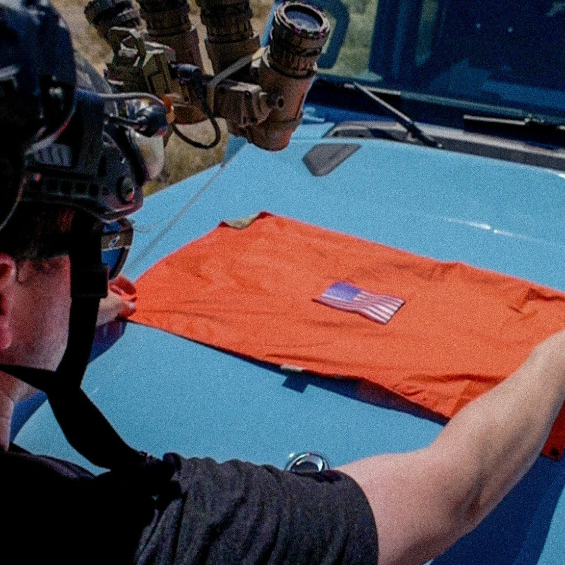 Person folding an orange t-shirt with a flag design on a blue vehicle