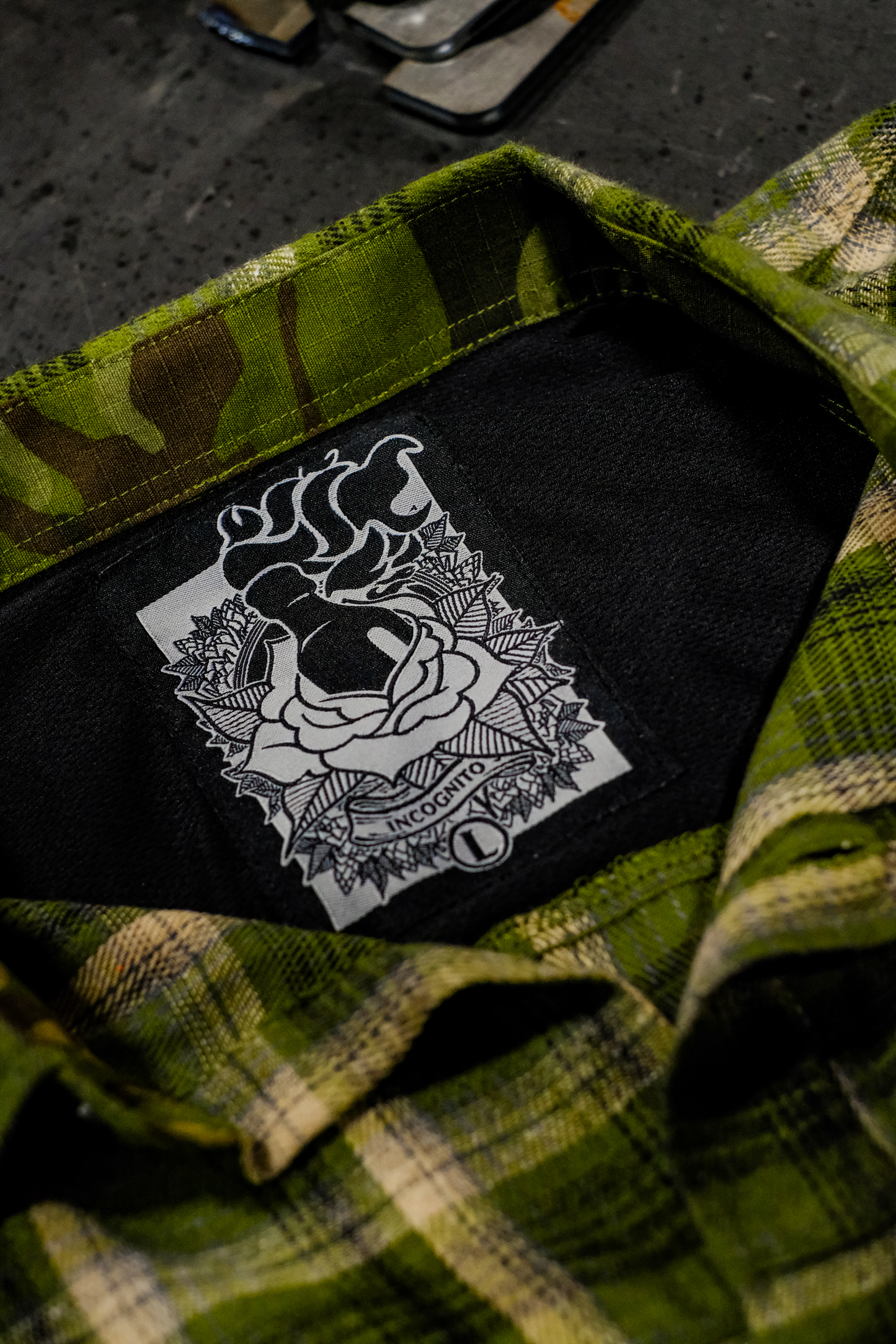 Green camouflage shirt with a black patch featuring a white design on a dark surface.