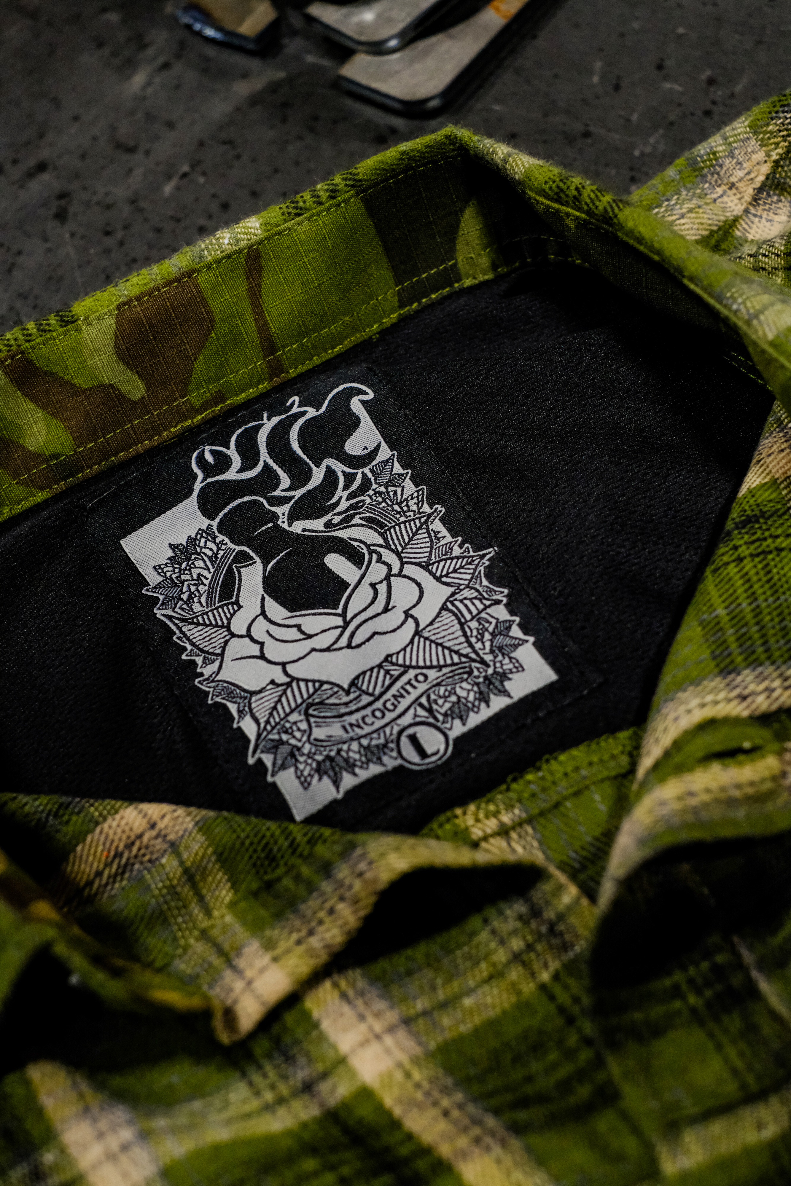 Green camouflage shirt with a black patch featuring a white design on a dark surface.